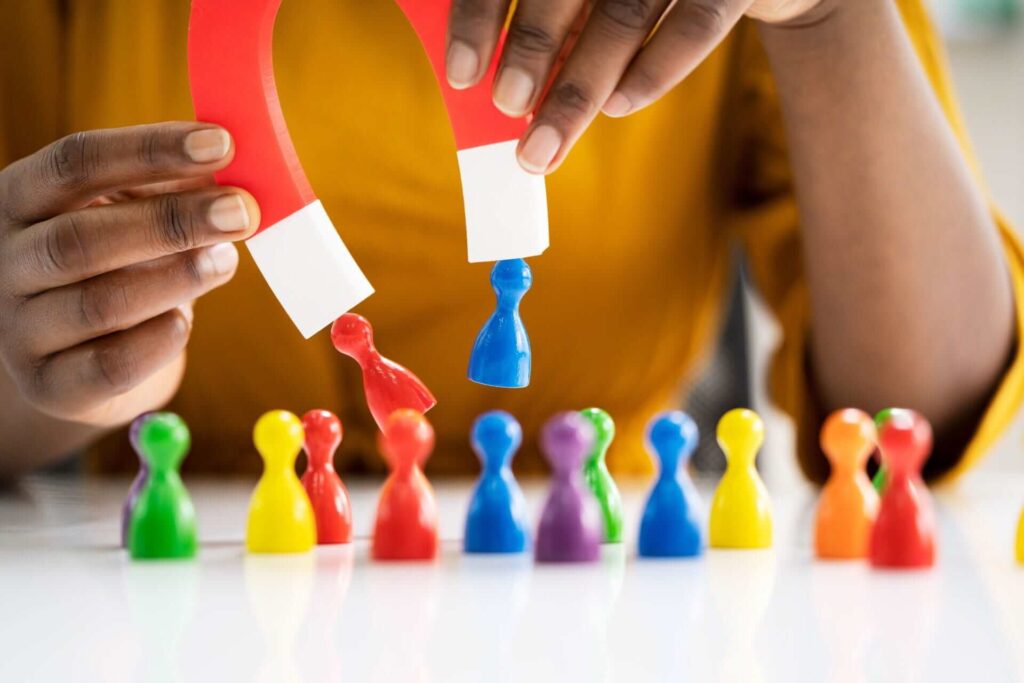 A man holding a magnet which is attracting some toy people towards it